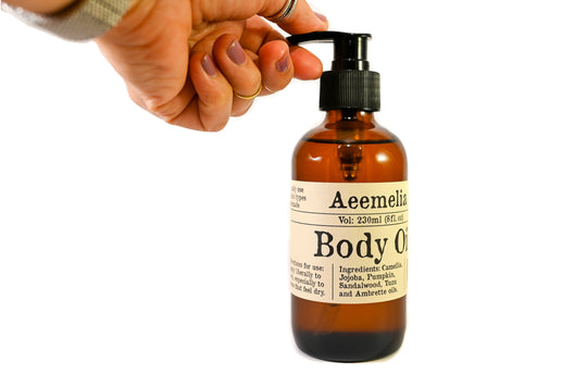 Aeemelia Body Oil is an excellent moisturizer, rich with the nutrients and antioxidants naturally present in plants to promote radiant skin health. Black pump top 8 oz amber glass bottle with white and black label.  Suitable for all skin types (including sensitive skin). With hand for reference to show the size of the bottle.