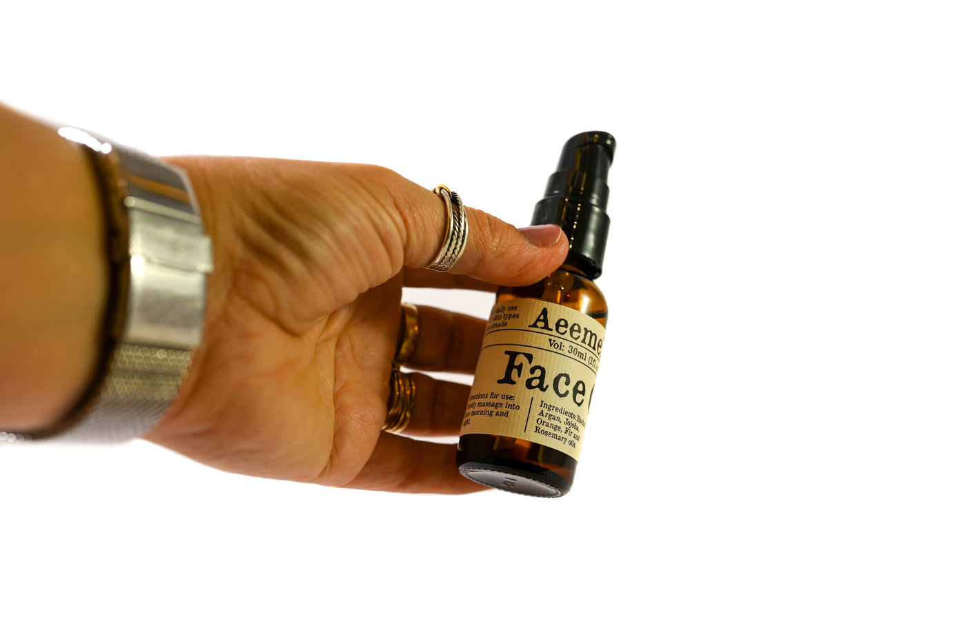 Aeemelia face oil, a nourishing, moisturizing, protective face oil steeped with the benefits of Baobab and Argan oils. Black pump top 1oz amber glass bottle with white and black label. Suitable for all skin types (including sensitive skin). Shown with a hand for reference on the size of the bottle. 